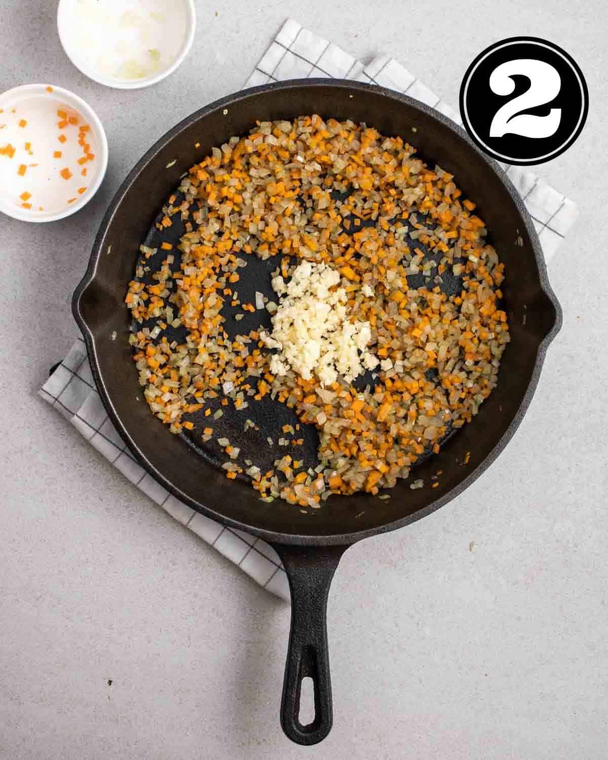 Adding garlic to a pan of cooked vegetables with 2 ramekin beside.