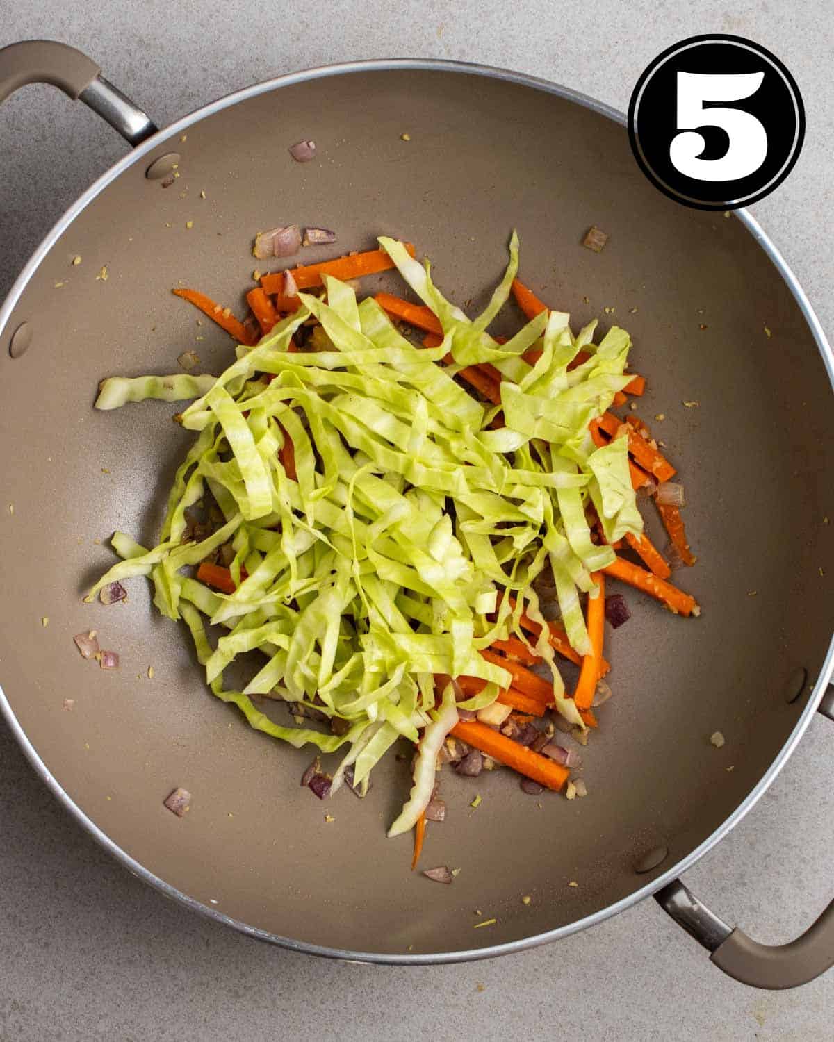 Adding cabbage to a pan of cooked carrots and aromatics.