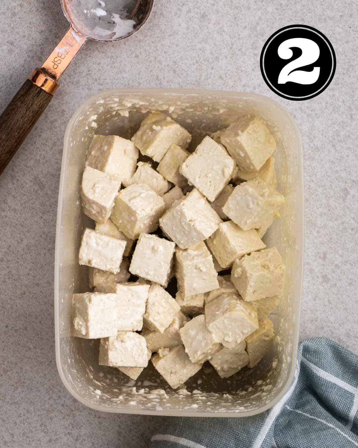 Tofu cubes coated in corn starch in a container with a tablespoon beside.