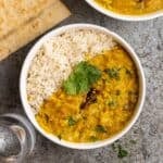 A bowl of rice served with dal with naan, bowl of dal, and glass of water beside.