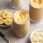 2 glasses of smoothie with banana slices, glass of milk and oats beside.