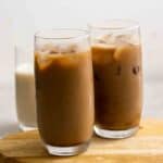 2 glasses of iced coffee on a wooden board and a glass of milk in the background.