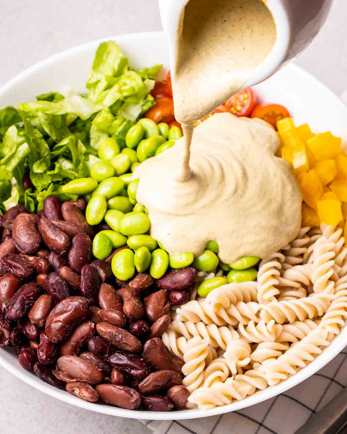 Pouring dressing over salad ingredients in a mixing bowl.