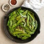 A pan of stir-fried snow peas with chili flakes and sesame seeds beside.