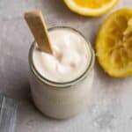 A jar of tofu sour cream with a wooden spoon with 2 lemon halves in the background.
