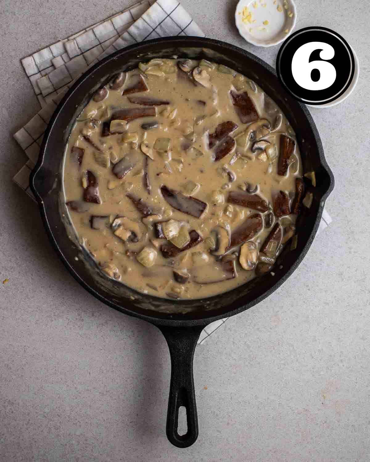 Vegan stroganoff in a cast-iron skillet on a white folded teacloth with 2 sauce dishes beside.