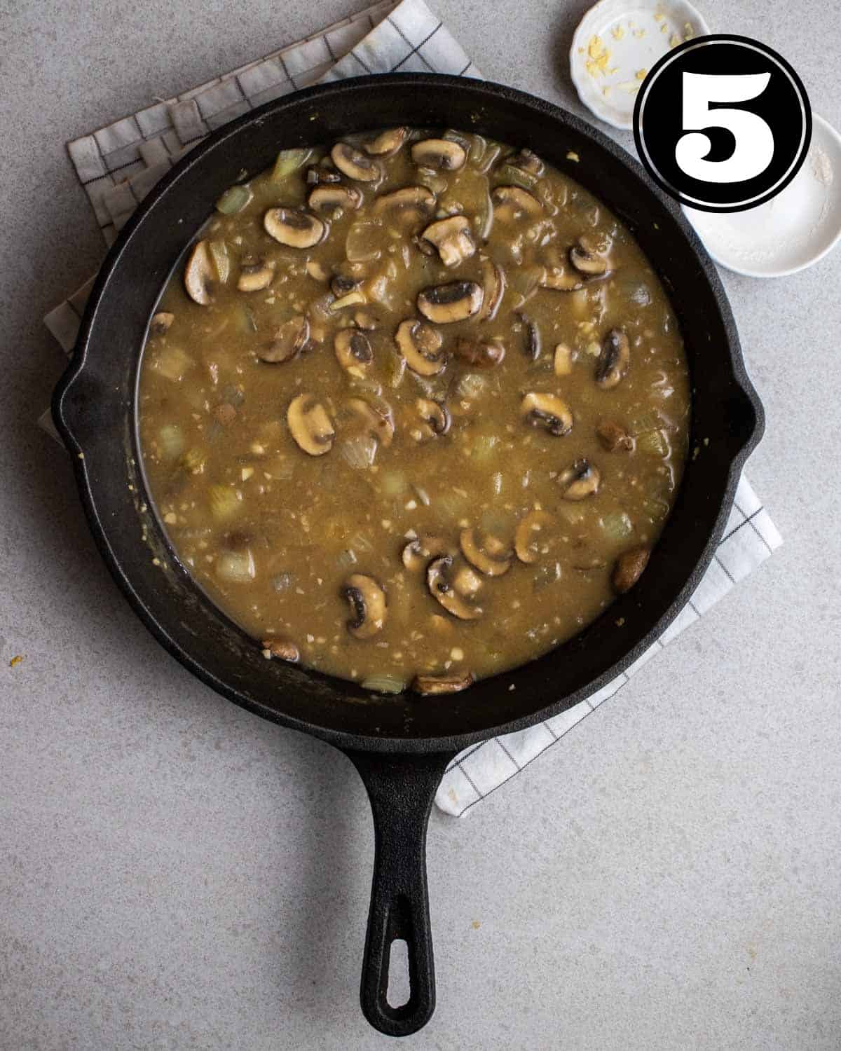 Broth, cooked mushrooms, and onion in a cast-iron skillet on a white folded teacloth.