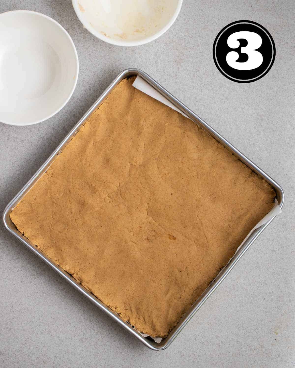 Dough of protein bars pressed into a square pan lined with parchment paper.