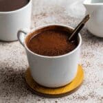 2 mugs of protein hot chocolate served with a teaspoon.
