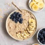 A bowl of oats served with a spoon with banana slices and blueberries beside.