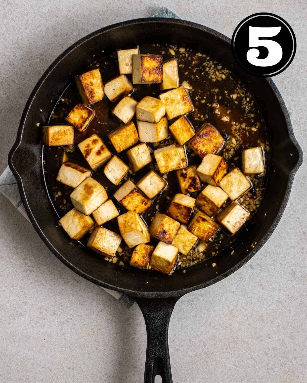 Simmering tofu in adobo sauce in a cast iron skillet.