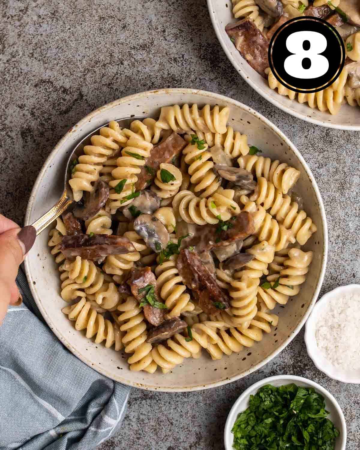 Stirring a plate of vegan stroganoff with pasta with a spoon.