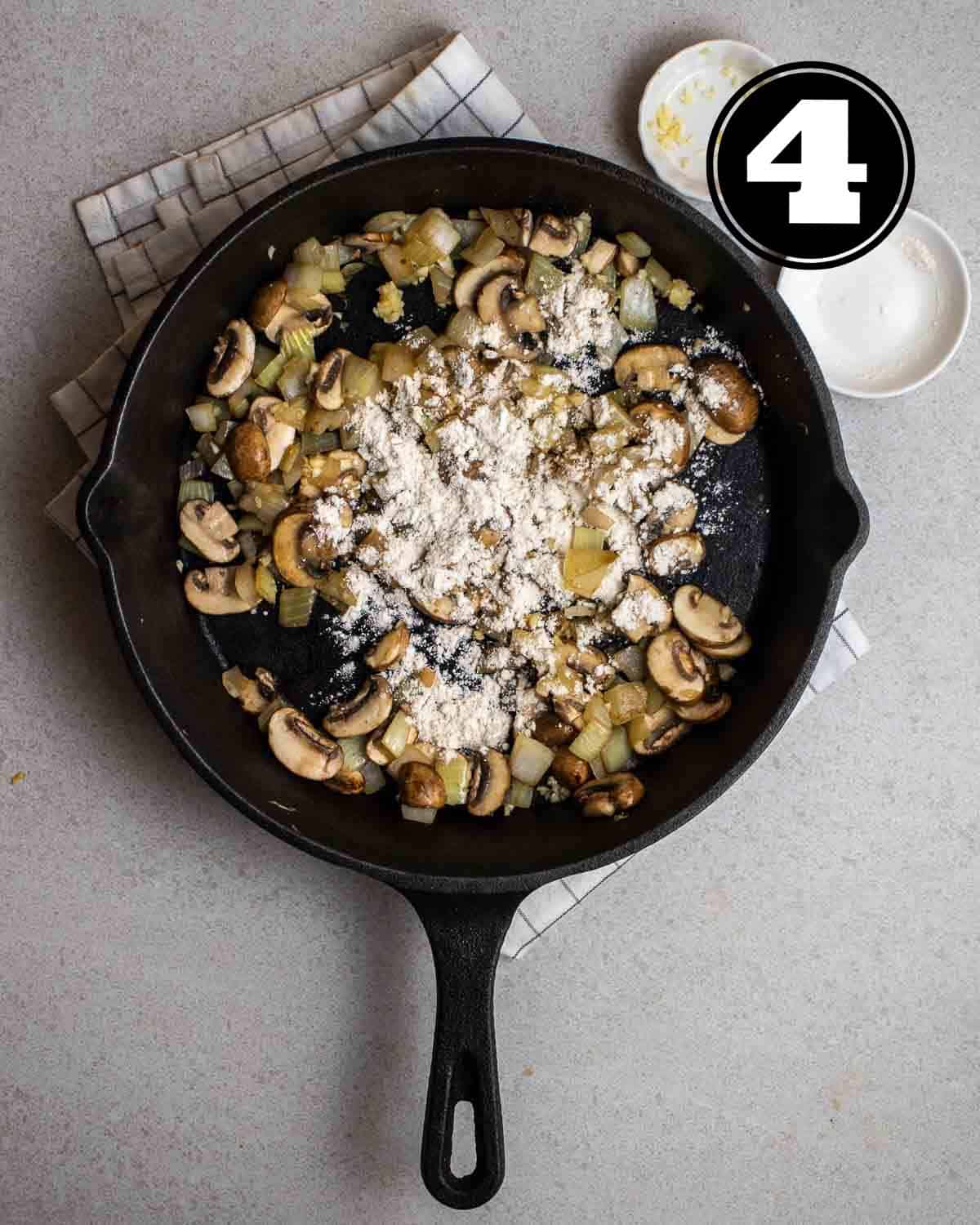 Adding flour and minced garlic to a pan of cooked mushrooms and onion.