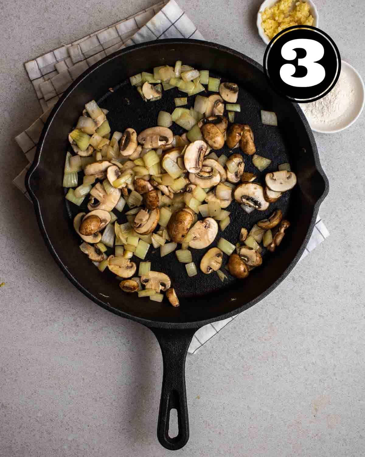 Cooked mushrooms and onion in a cast iron skillet with flour and minced garlic beside.