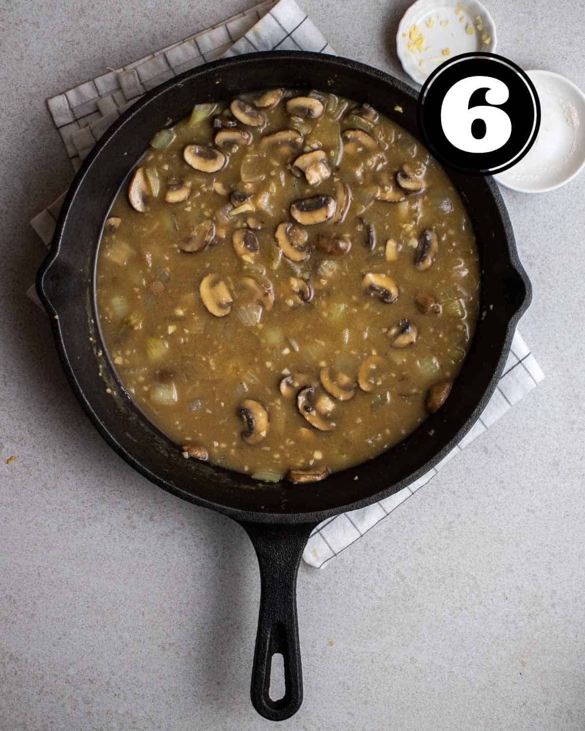 Broth for vegan stroganoff in a cast iron skillet on a white folded teacloth.