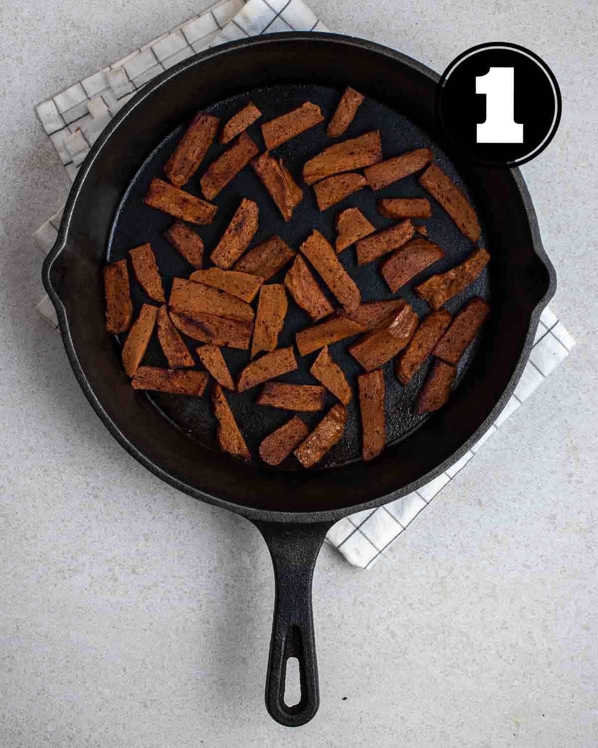 Seared seitan steak in a cast iron skillet on a white folded checkered teacloth.