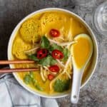 A bowl of laksa served with a pair of chopsticks and a ceramic spoon beside.