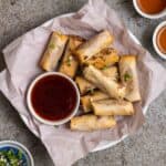 A plate of lumpia on a lined parchment paper served with soy sauce.