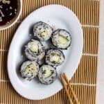 A plate of cucumber maki with a pair of chopsticks and soy sauce beside.
