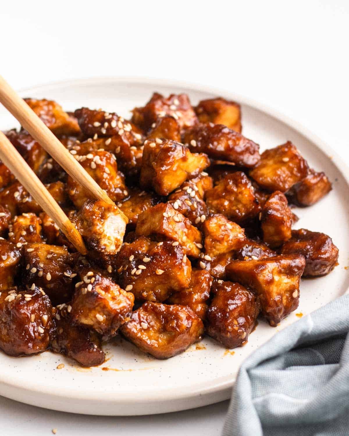 Taking a piece of hoisin tofu from a plate with a blue teacloth beside.