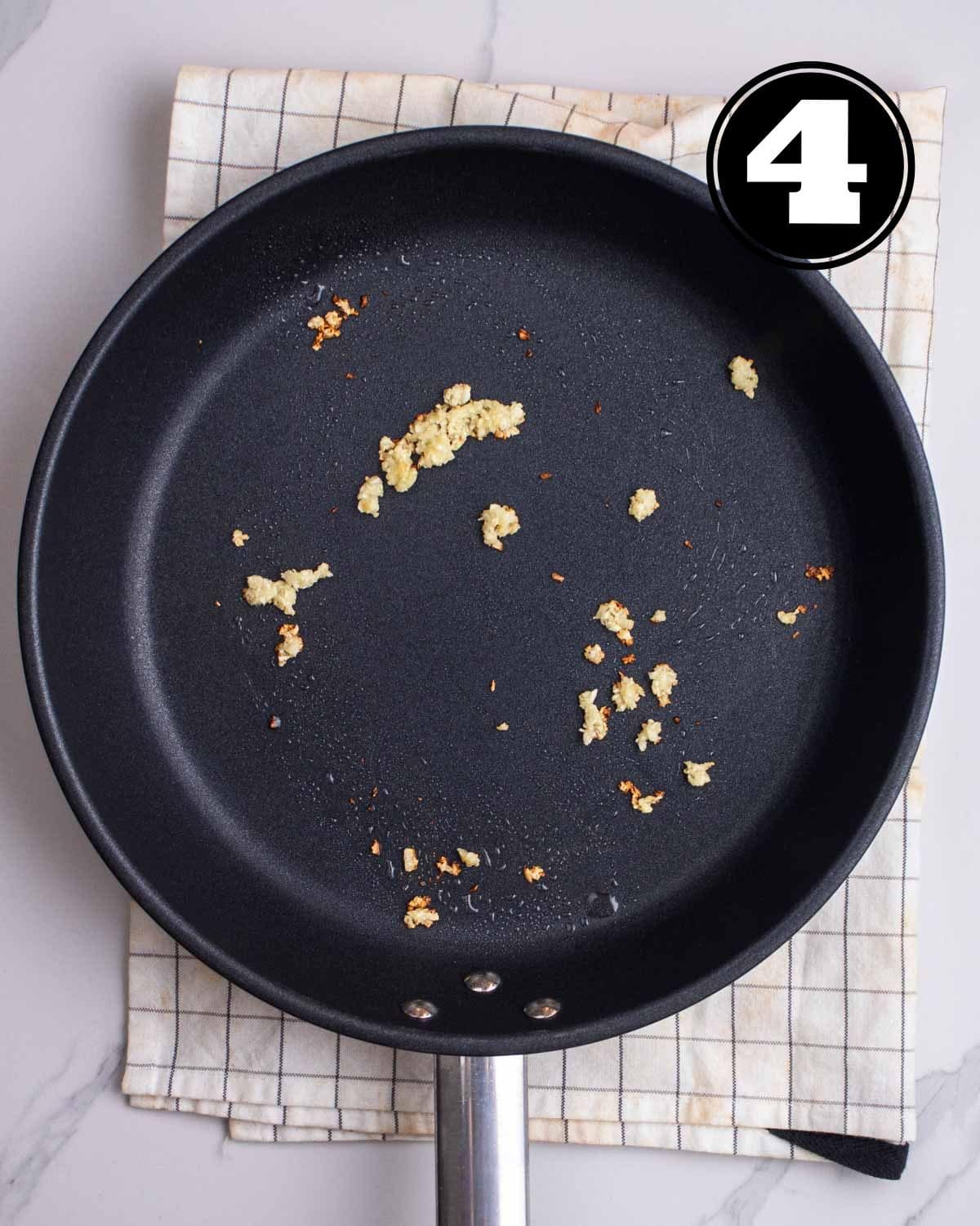 Fried garlic in a black non-stick pan on a folded white checkered teacloth.