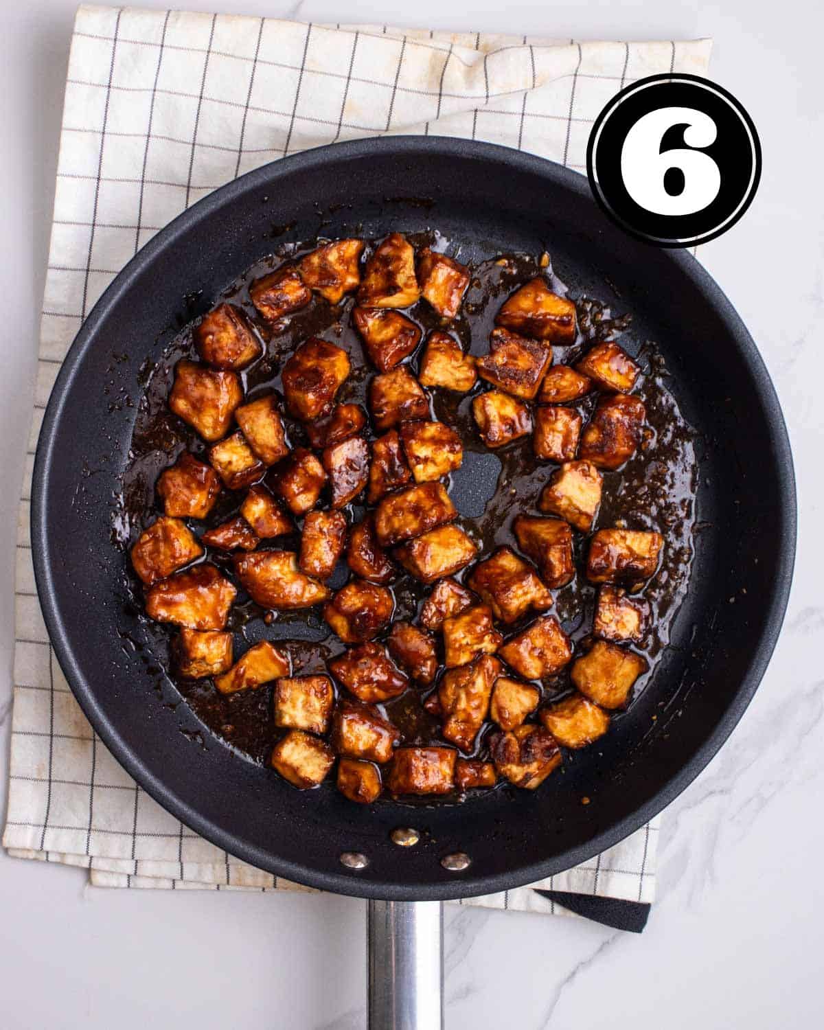 A pan of hoisin tofu in a black non-stick pan on a white folded checkered teacloth.
