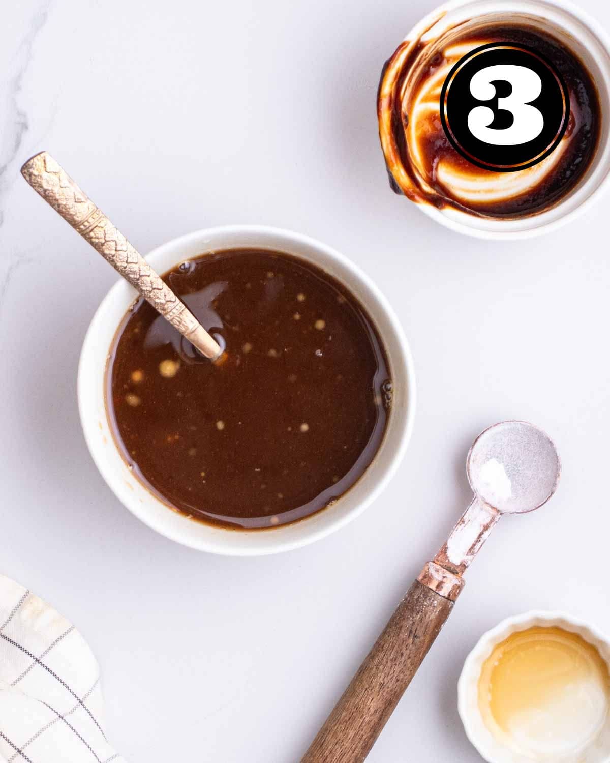 Sauce mixture in a ramekin with a teaspoon beside and an empty ramekin, a teaspoon, and a sauce dish beside.