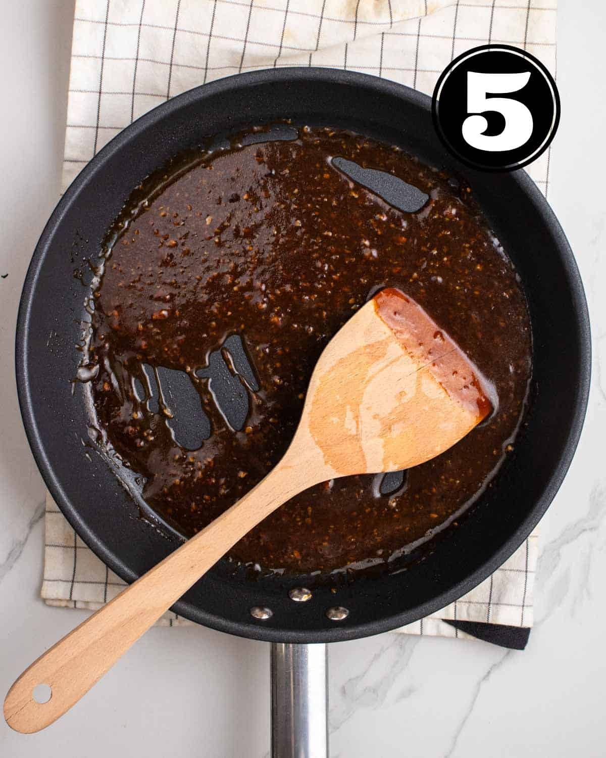 Thicken sauce in a non-stick pan with a wooden spatula beside.