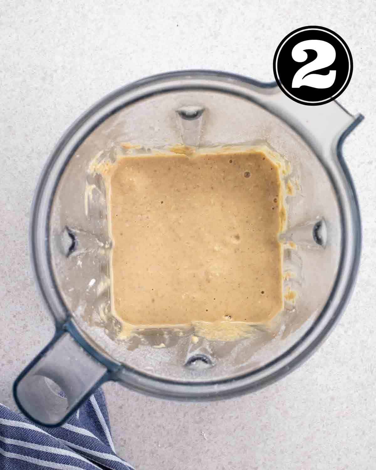 Pancake batter in a blender with a blue and white striped teacloth beside.