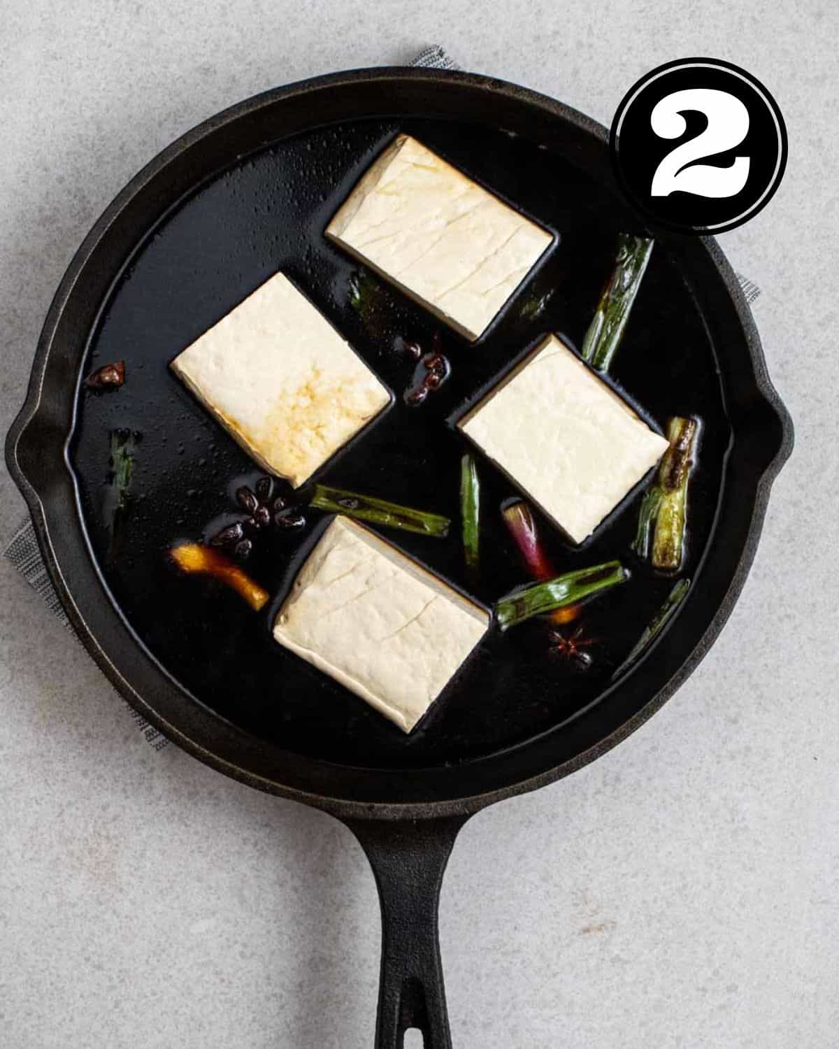 Adding chunks of tofu to soy sauce marinade in a cast iron skillet.