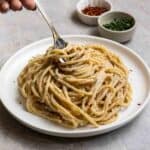 Holding some pasta with a fork with chopped parsley and chili flakes in the background.