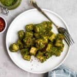 A plate of pesto tofu with a fork beside with chili flakes and jar of pesto beside.