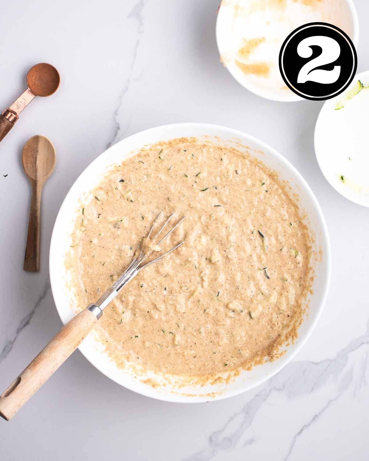 Muffin batter in a white bowl with a whisk. 