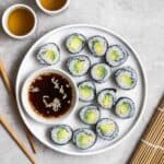 A plate of avocado maki slices served with soy sauce with a pair of chopsticks and 2 cups of tea beside.