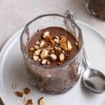 A glass of protein pudding served with a teaspoon on a blue plate.
