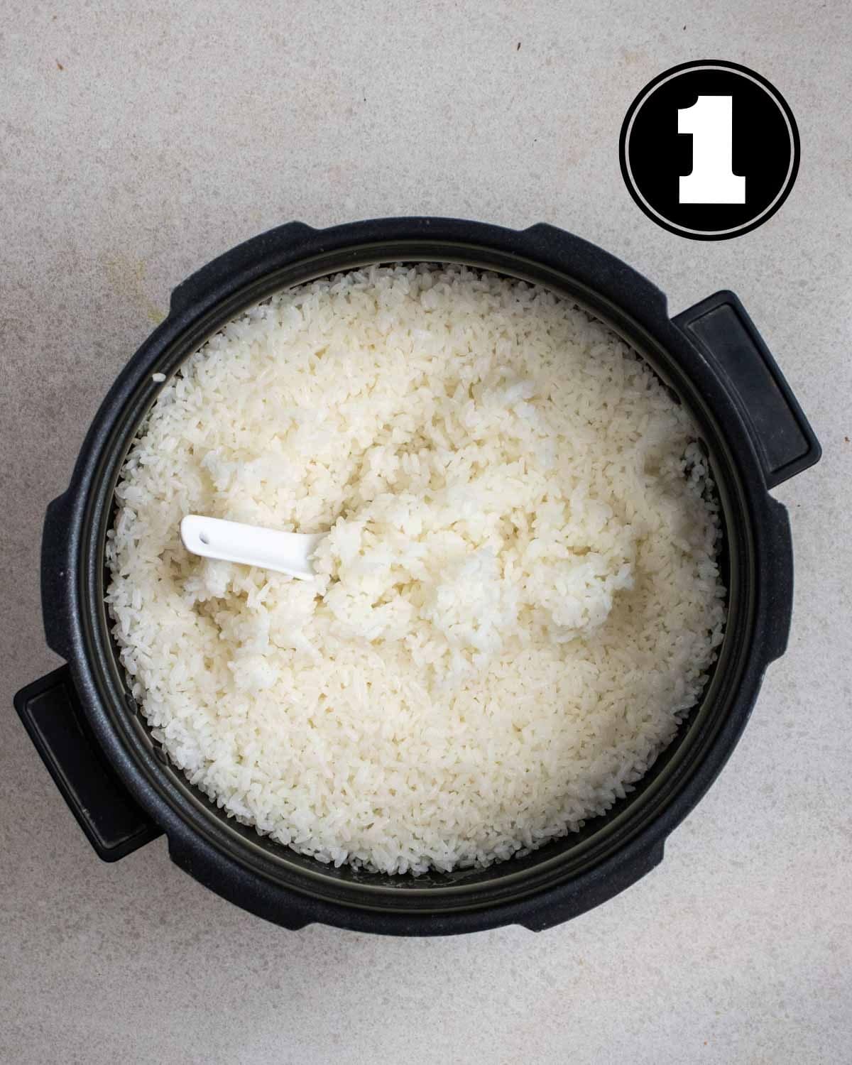 Cooked rice in a pot with a white ceramic spoon inside.