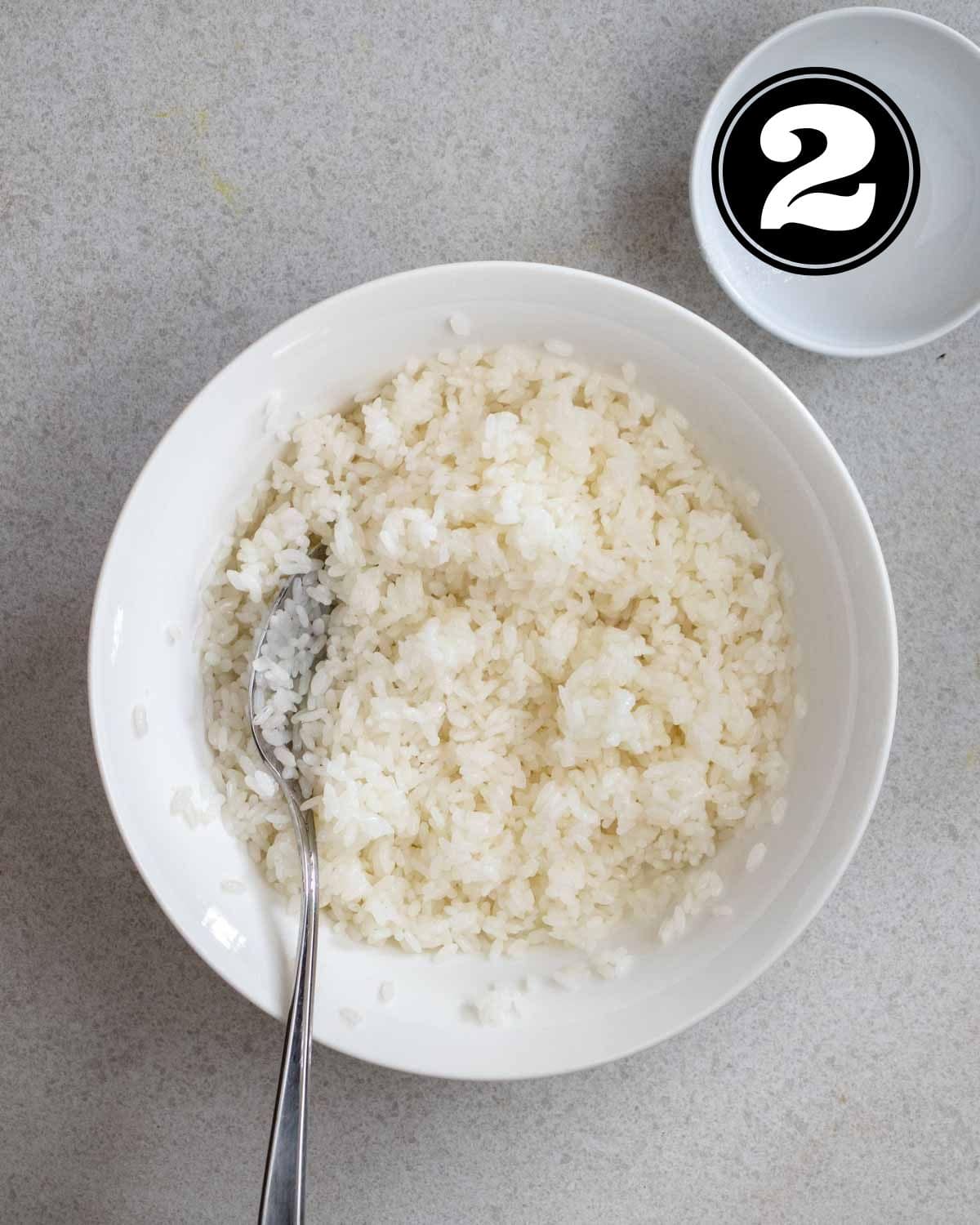 Sushi rice in a bowl with a spoon beside.