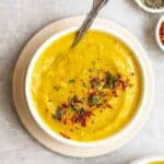 A bowl of lentil carrot soup served with a spoon on a saucer.