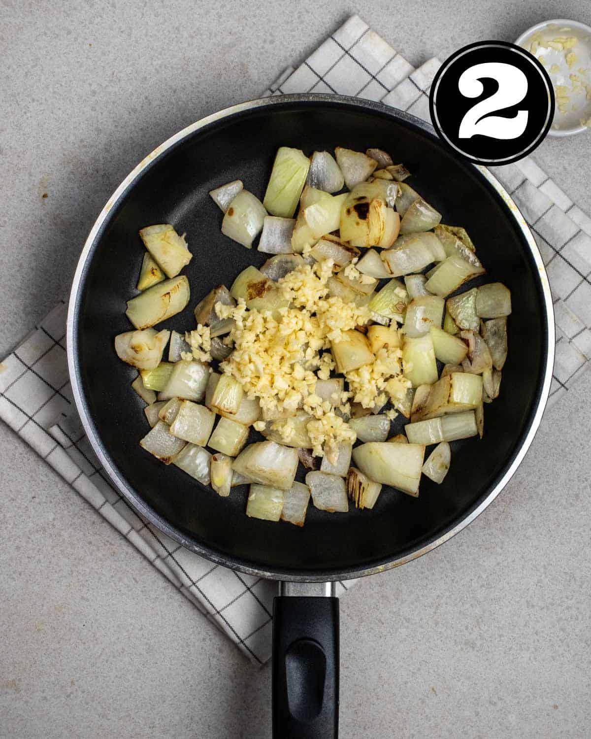 Cooked onion and garlic in a non-stick pan on a white folded teacloth.