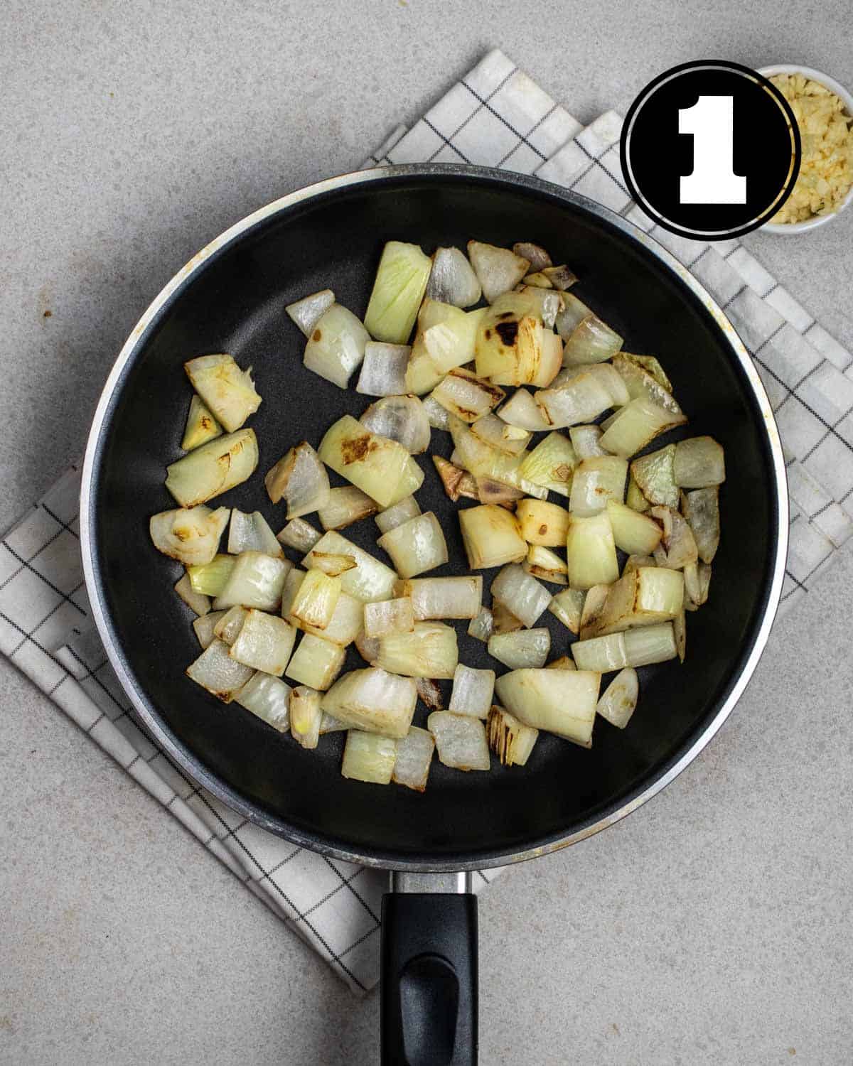 Cooked onion in a non-stick pan on a white folded teacloth.