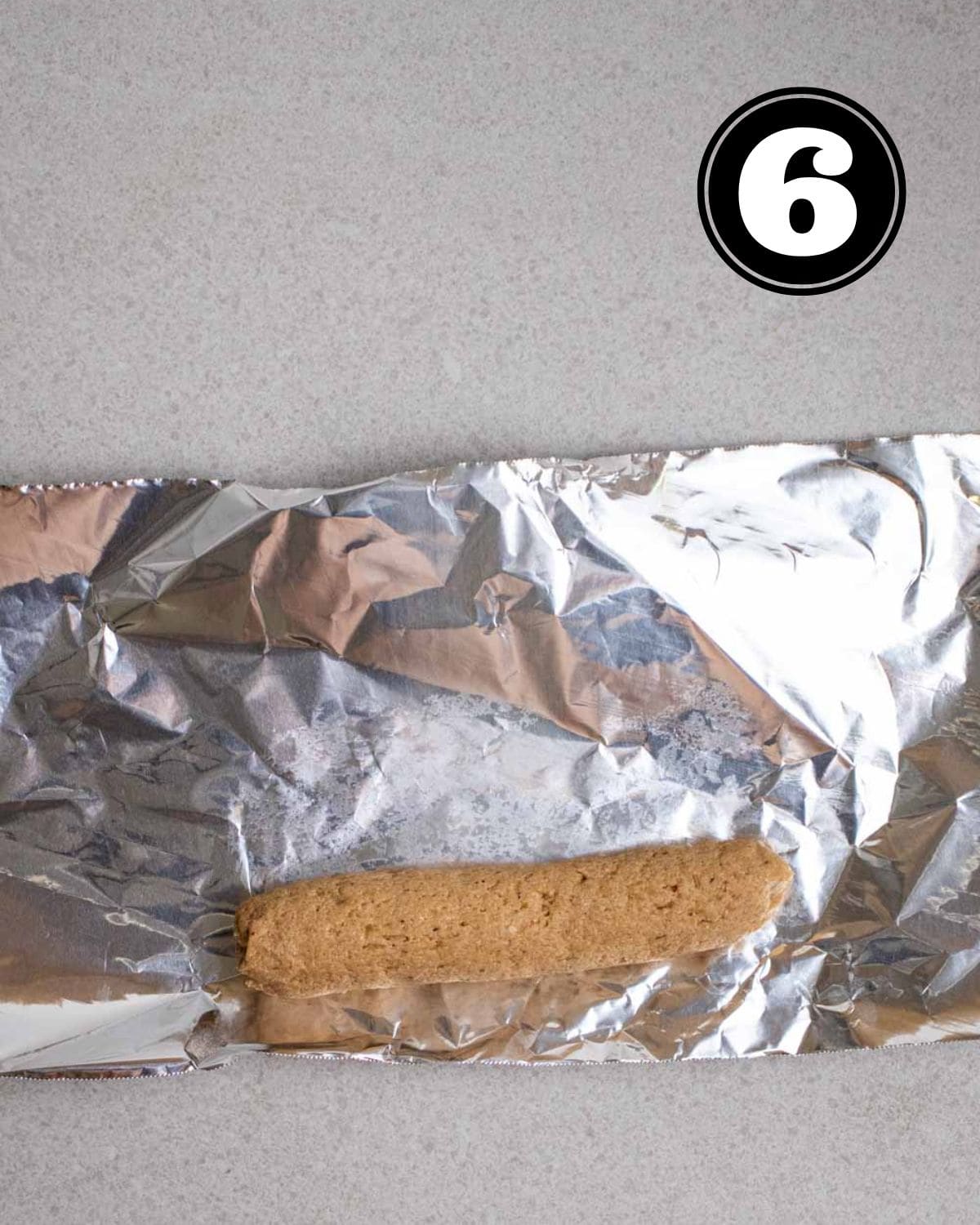 Shaped seitan sausage on a piece of aluminum foil.