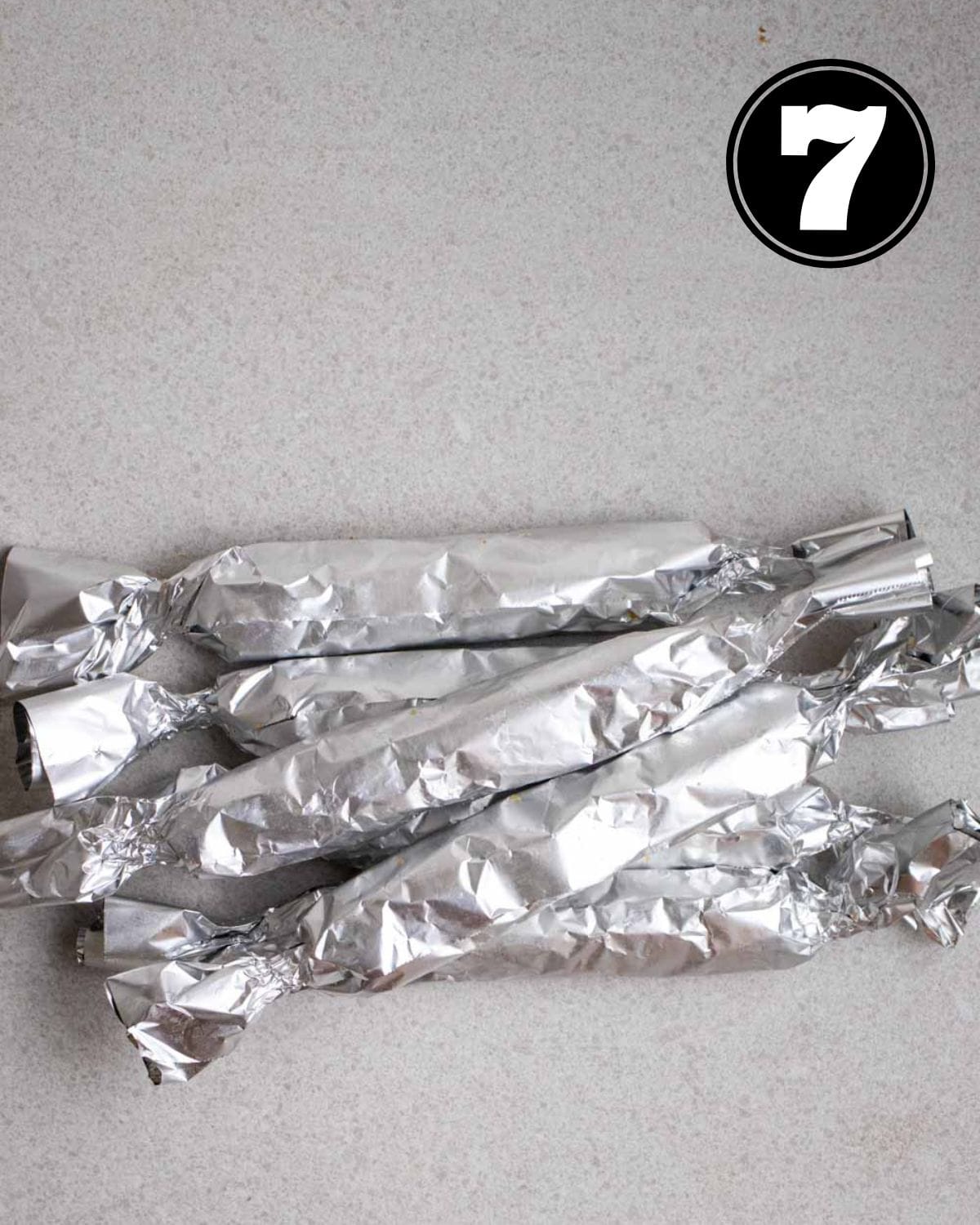 Seitan sausages wrapped in aluminum foil on a grey background.