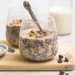 2 glasses of oatmeal chia pudding on a wooden board with a jar of milk in the background.