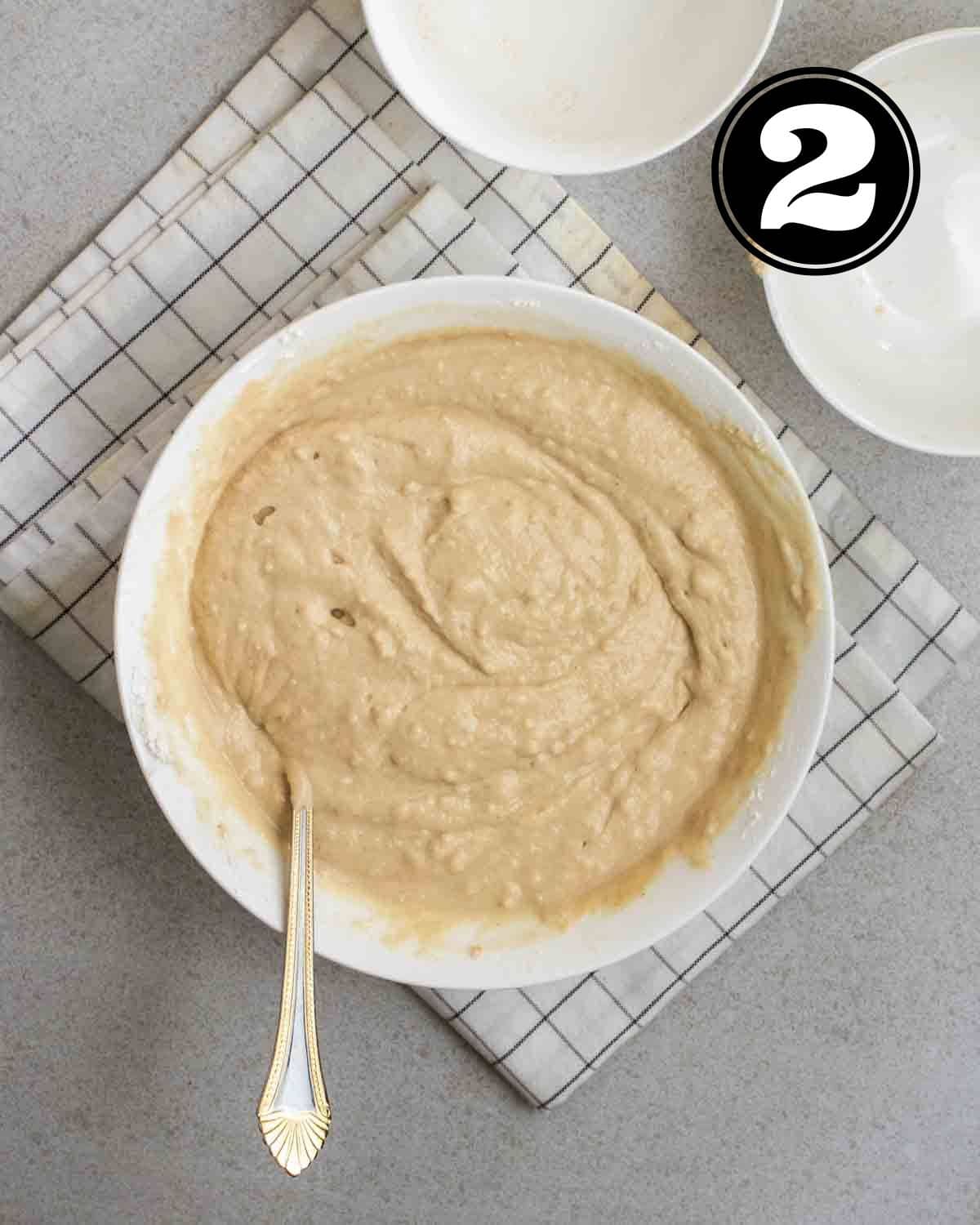 Batter for protein pancakes in a bowl with a fork. There are 2 empty ramekins beside.