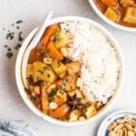 A bowl of Massaman curry served with rice with a bowl of curry and peanuts beside.