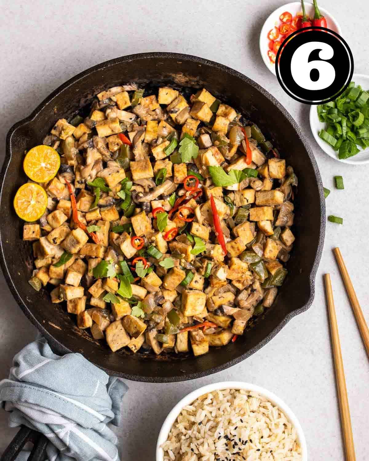 A pan of tofu sisig with chopsticks, chopped chilies and green onions, and a bowl of rice beside.