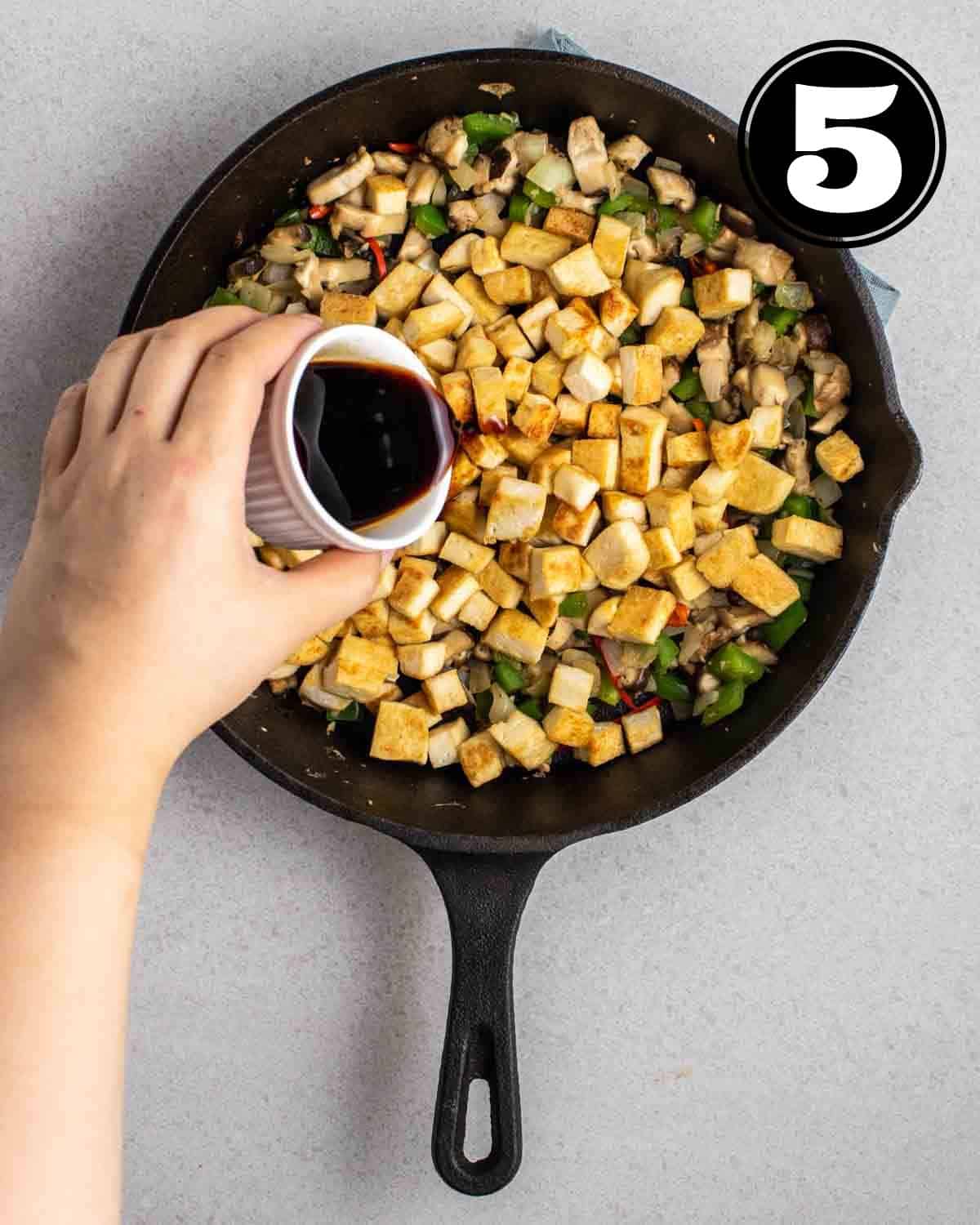 Adding stir-fry sauce into a pan of cooked tofu and vegetables.