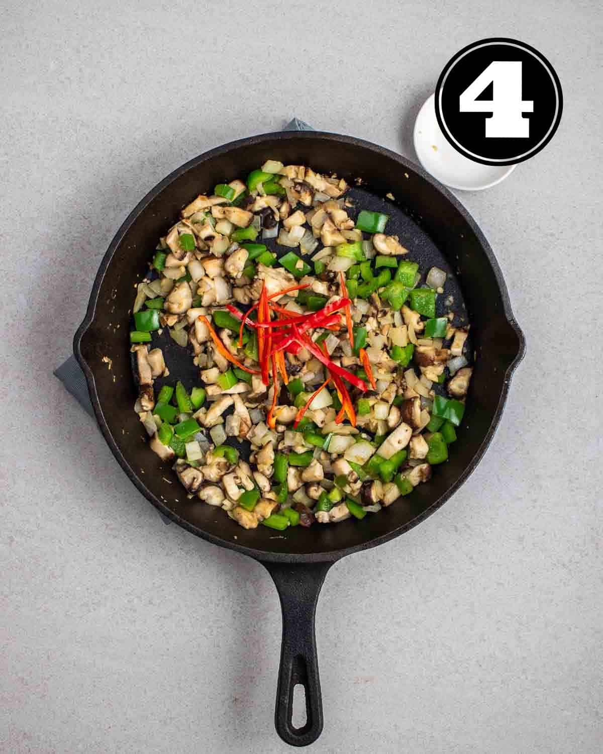 Cooked onion, mushrooms, peppers, and chilies in a cast iron pan.