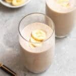 2 glasses of tofu smoothie with a plate of banana slices and a teaspoon beside.