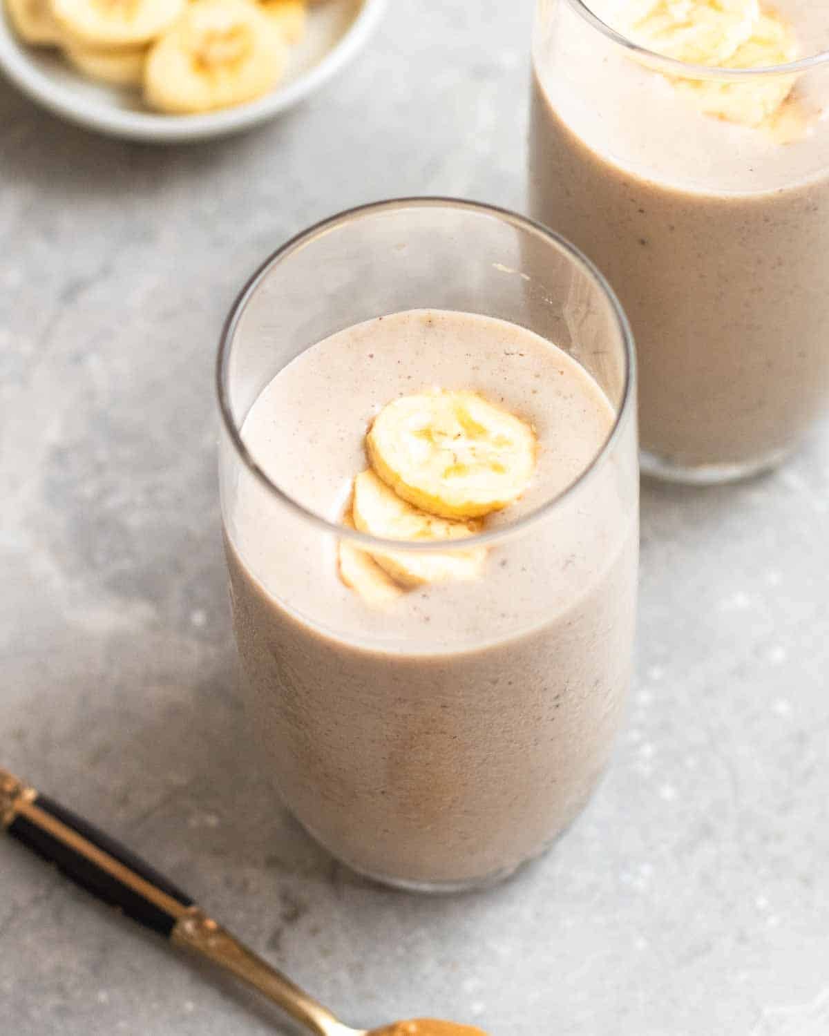 2 glasses of tofu smoothies with a plate of banana slices and a teaspoon beside.